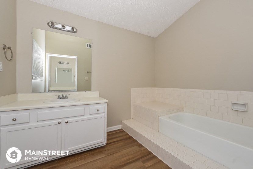 the master bathroom has a tub and a sink and a mirror