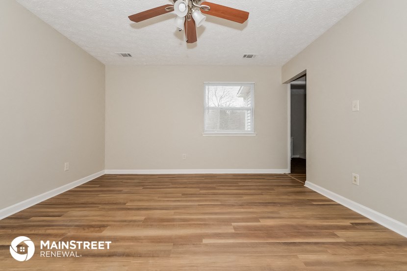 the spacious living room with hardwood flooring and a ceiling fan