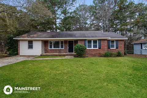 front view of a small brick house with green grass and trees