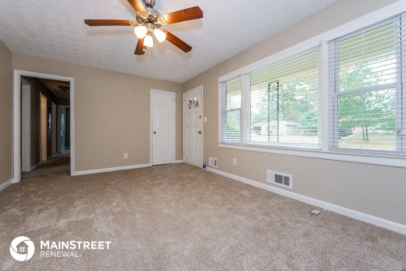 an empty living room with a ceiling fan and large windows
