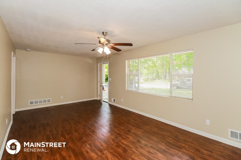 the spacious living room with wood flooring and ceiling fan