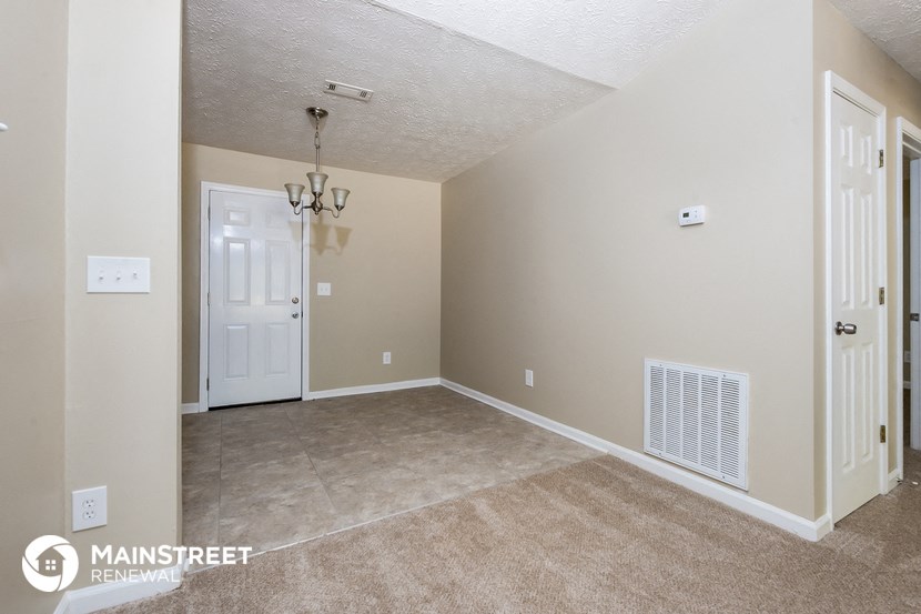 an empty living room with a white door and beige carpet