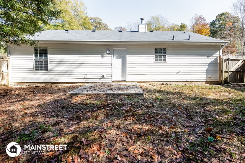 the backyard of a white house with a yard covered in fallen leaves