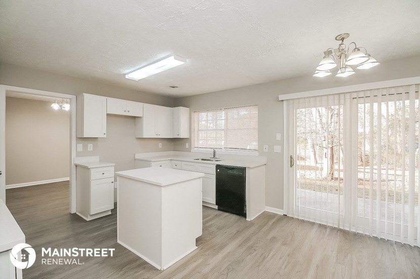 the kitchen of this home has white cabinets and white appliances and a sliding glass door