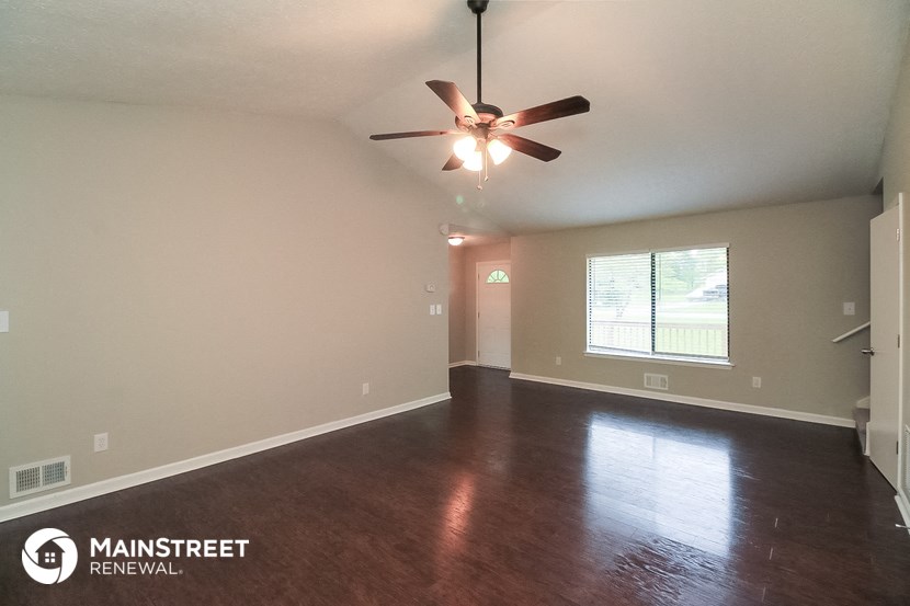 the spacious living room with hardwood flooring and ceiling fan
