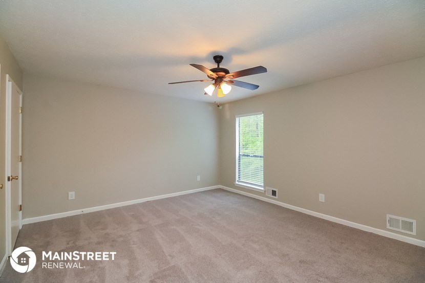 the spacious living room with ceiling fan and carpeting