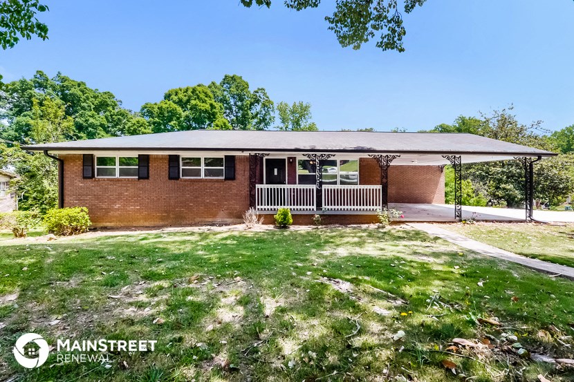 a small brick house with a porch and a lawn