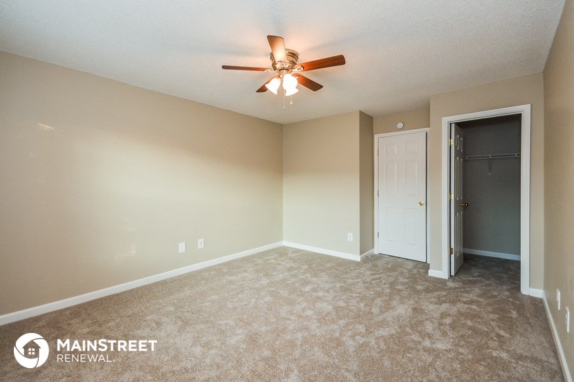 an empty living room with a ceiling fan and a door to a closet