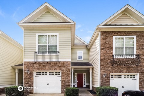 two story house with white garage doors and a brick building