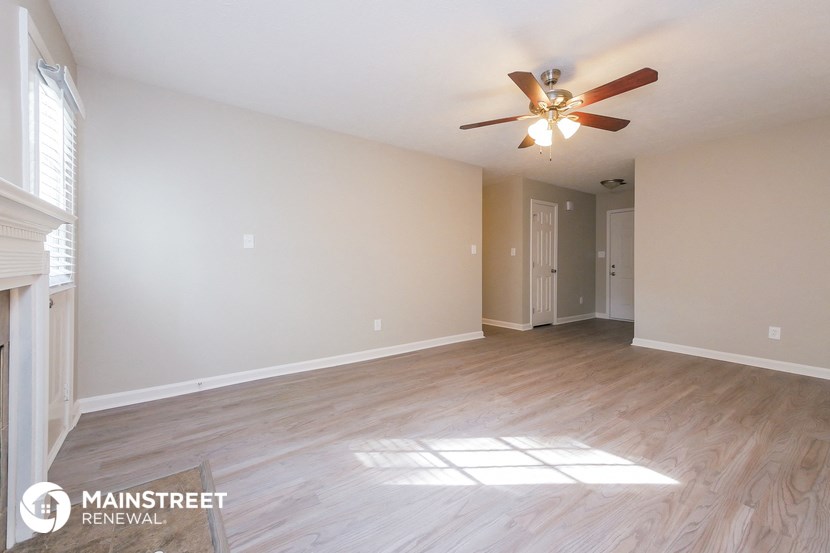 the spacious living room with hardwood floors and a ceiling fan
