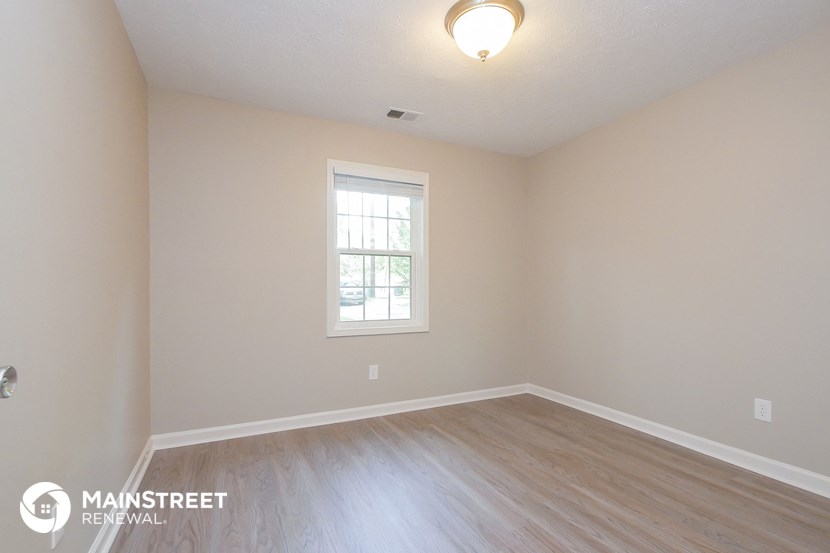 the spacious living room with wood flooring and a window