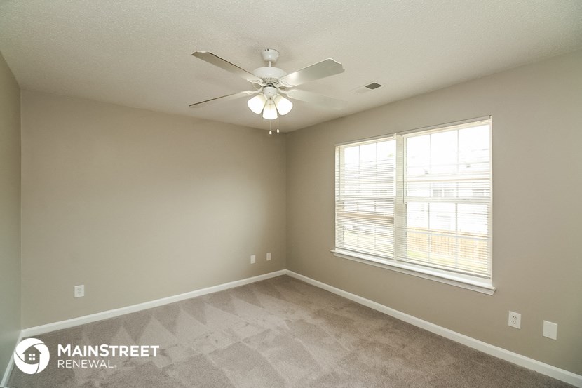 the spacious living room with a large window and a ceiling fan