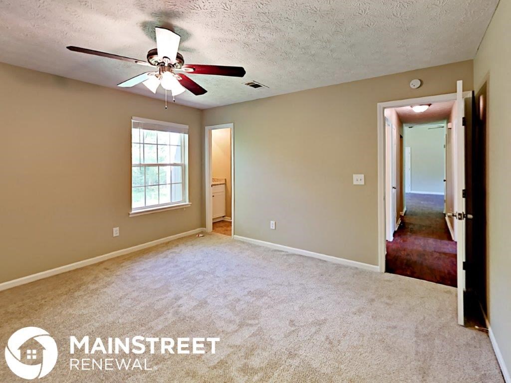 an empty living room with a ceiling fan and a door to a hallway
