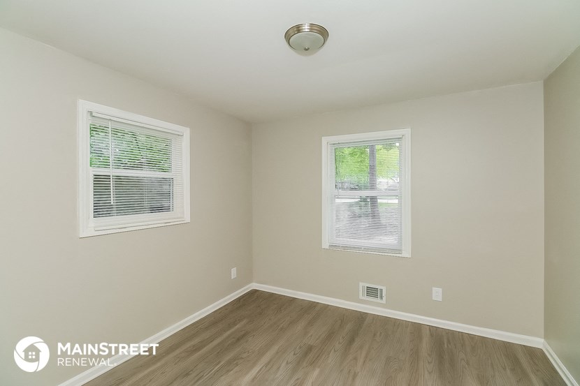the interior of an empty room with wood flooring and two windows