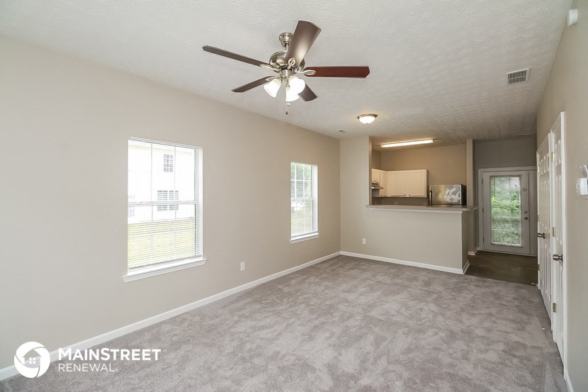 an empty living room with a ceiling fan and a kitchen