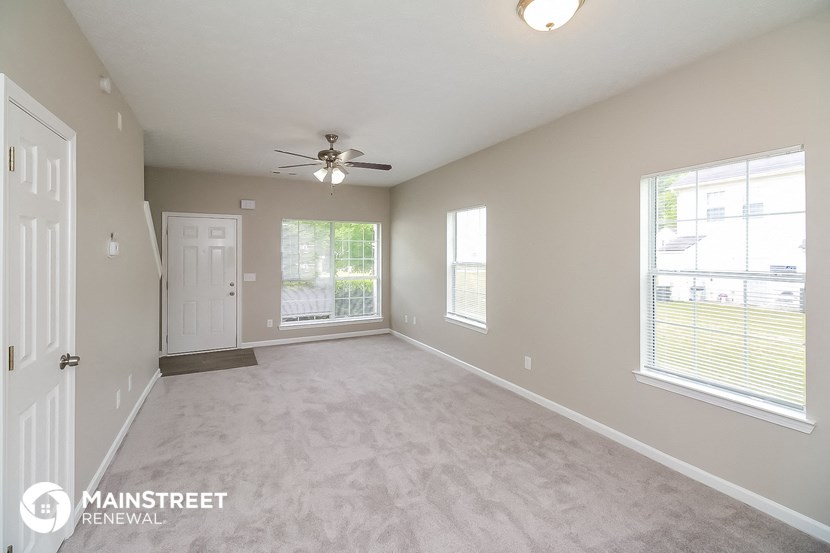 an empty living room with a ceiling fan and two windows