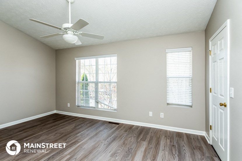 the spacious living room with hardwood flooring and a ceiling fan
