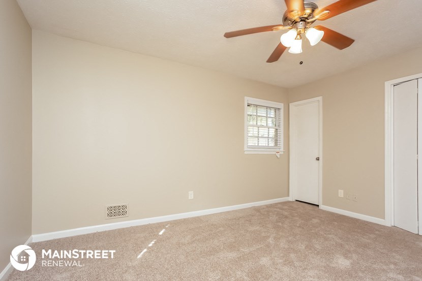 the spacious living room with ceiling fan and carpeting