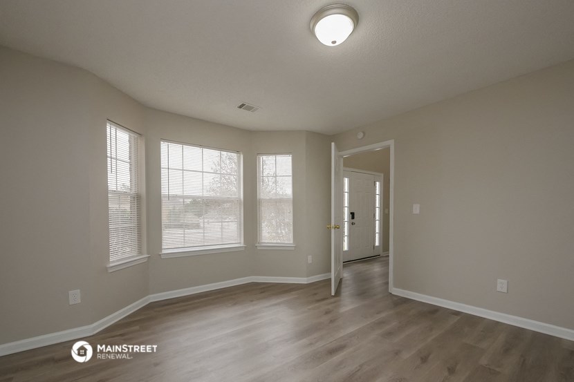the spacious living room of an apartment with wood flooring and windows