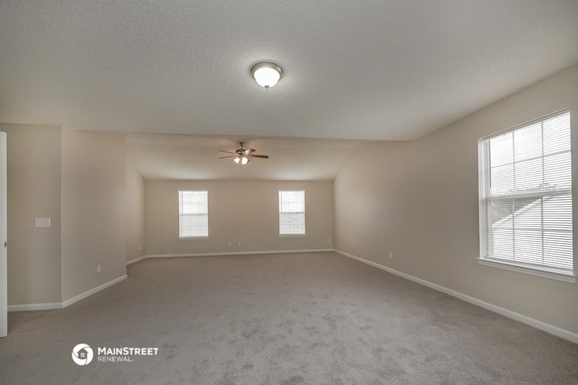 the spacious living room with ceiling fan and windows