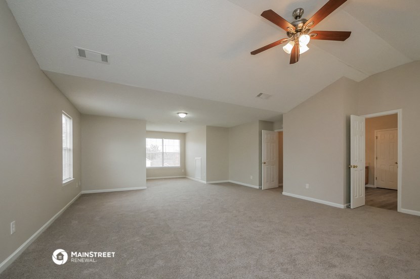 the spacious living room with ceiling fan and carpeting