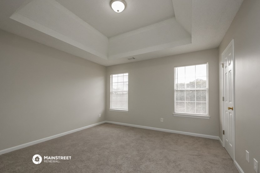 the spacious living room of this manufactured home has carpeted flooring and two windows