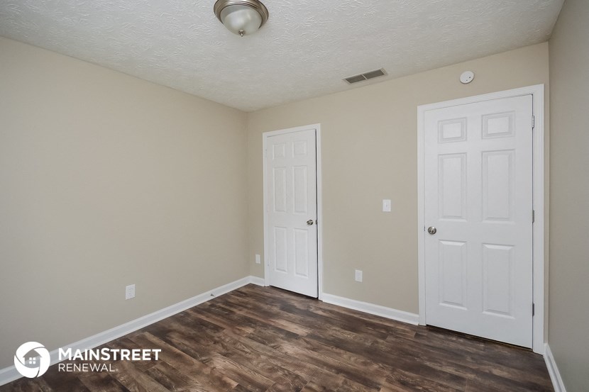 the spacious living room with two white doors and wood flooring