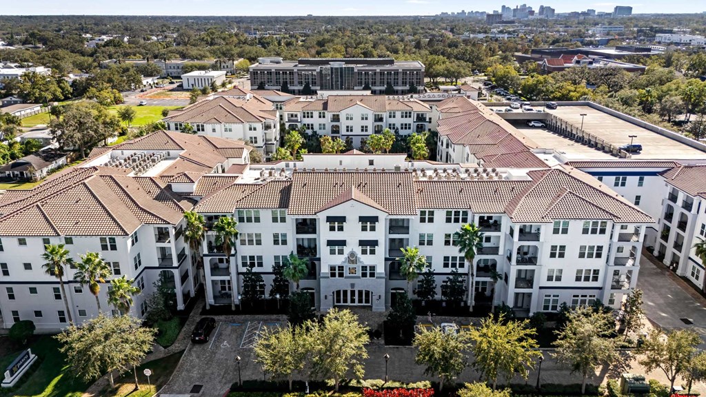 A large white building with a red roof is surrounded by trees and has a parking lot in front.
