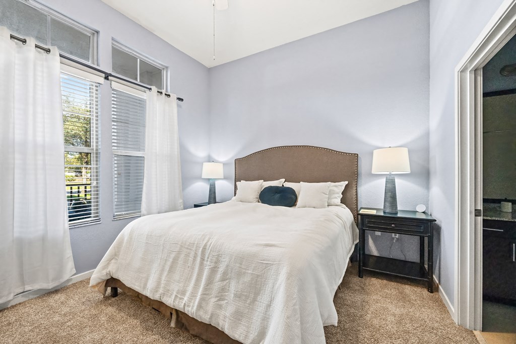 A bedroom with a bed, nightstand, and window with curtains.