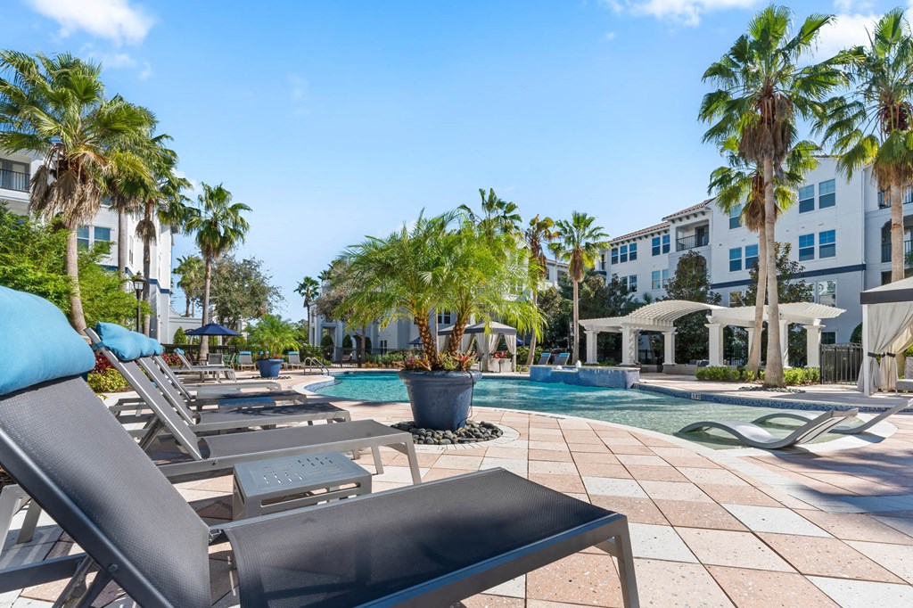 A pool area with sun loungers and palm trees.