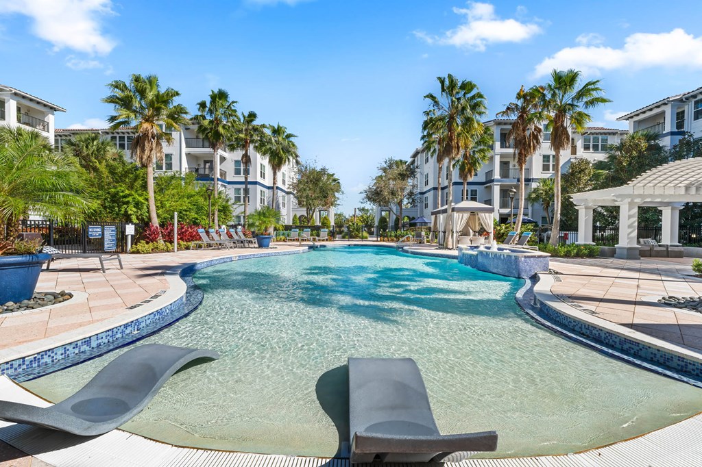 A large swimming pool with loungers and palm trees in the background.