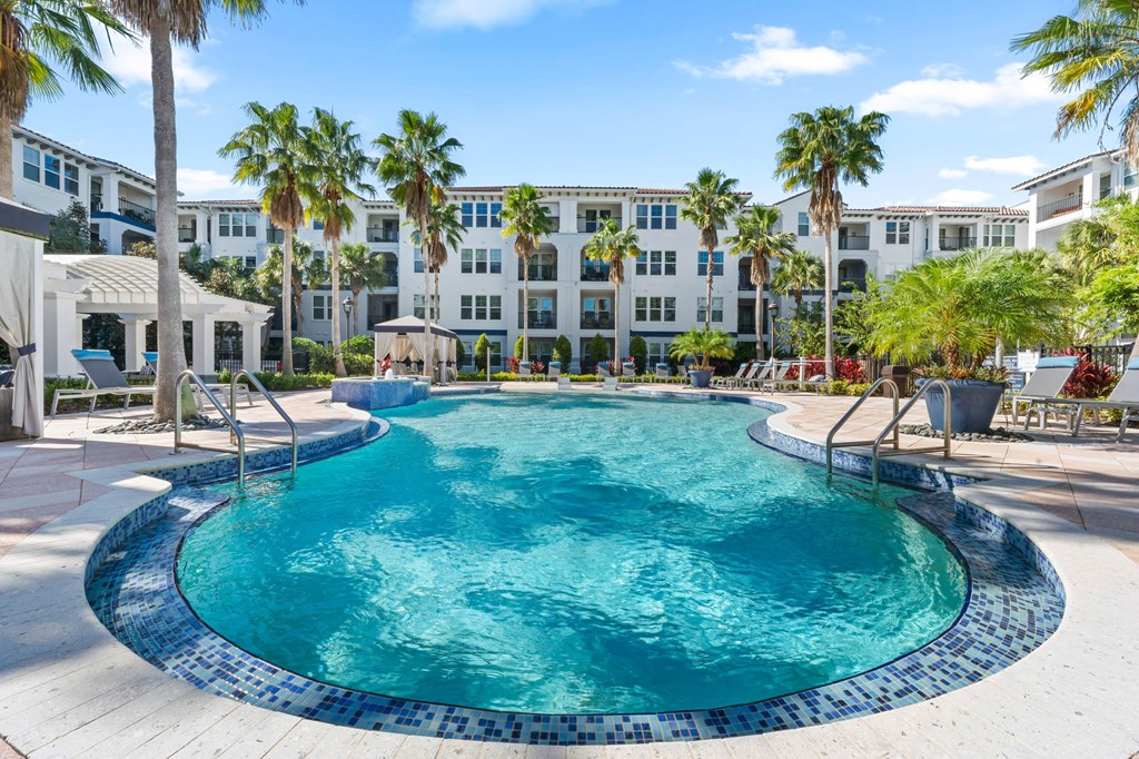 A swimming pool surrounded by palm trees and lounge chairs.