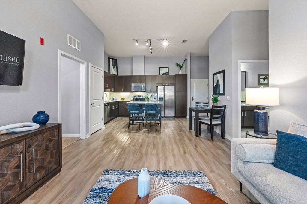 A living room with a couch, a dining table, and a kitchen area in the background.