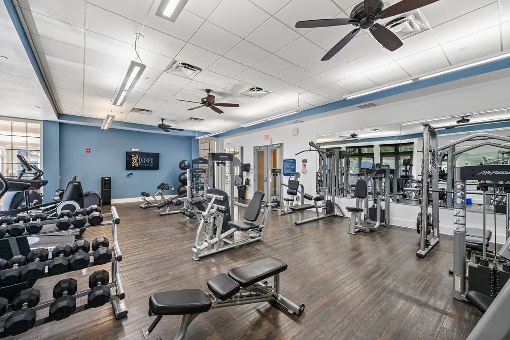 A gym with a variety of equipment including dumbbells, weight machines, and a bench.