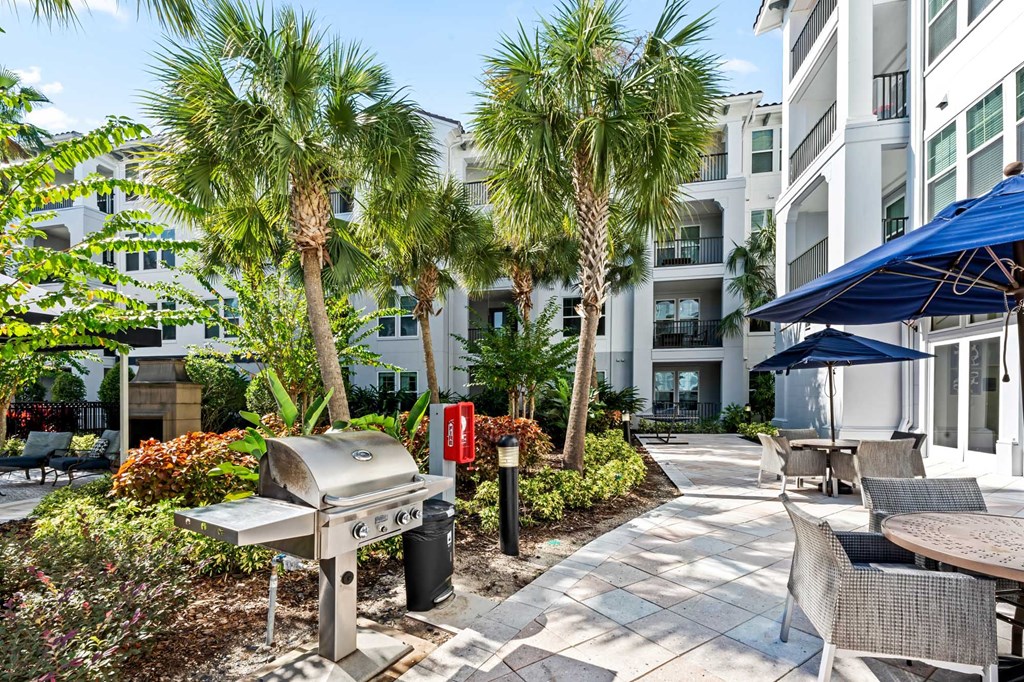 A patio with a grill and chairs is surrounded by palm trees.