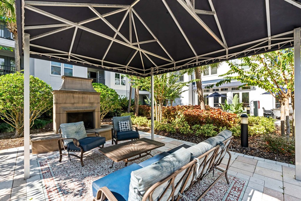 A patio with a fireplace and chairs under a black and white umbrella.