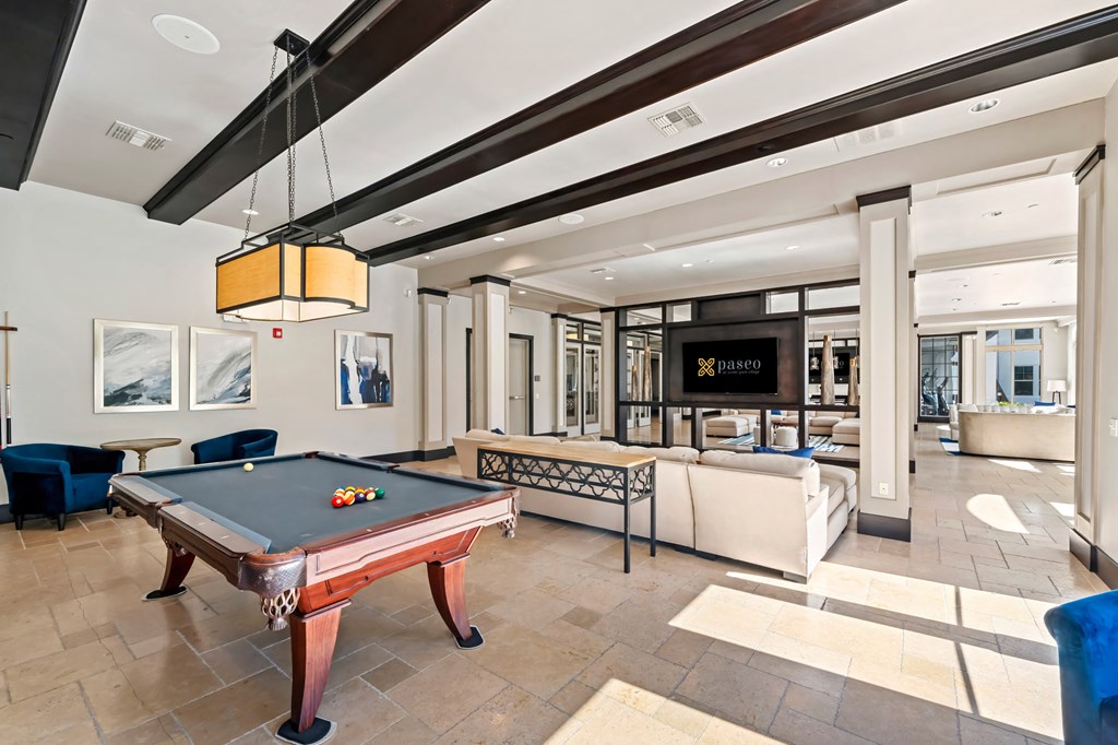 A billiard table is in the middle of a room with a blue chair and a white sofa.