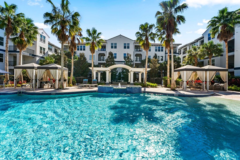A large swimming pool surrounded by palm trees and lounge chairs.