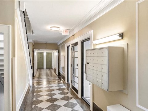 A hallway with a checkered floor and a mailbox on the wall.