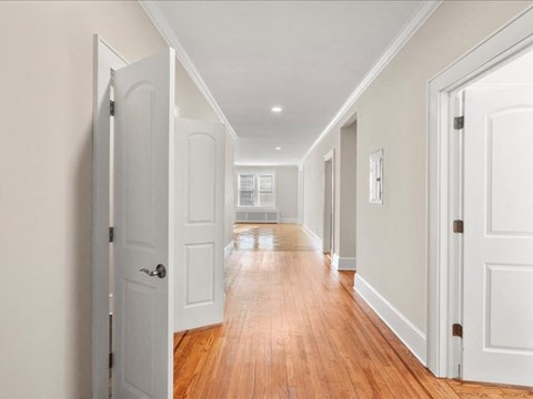 A long hallway with white doors and wood floors.