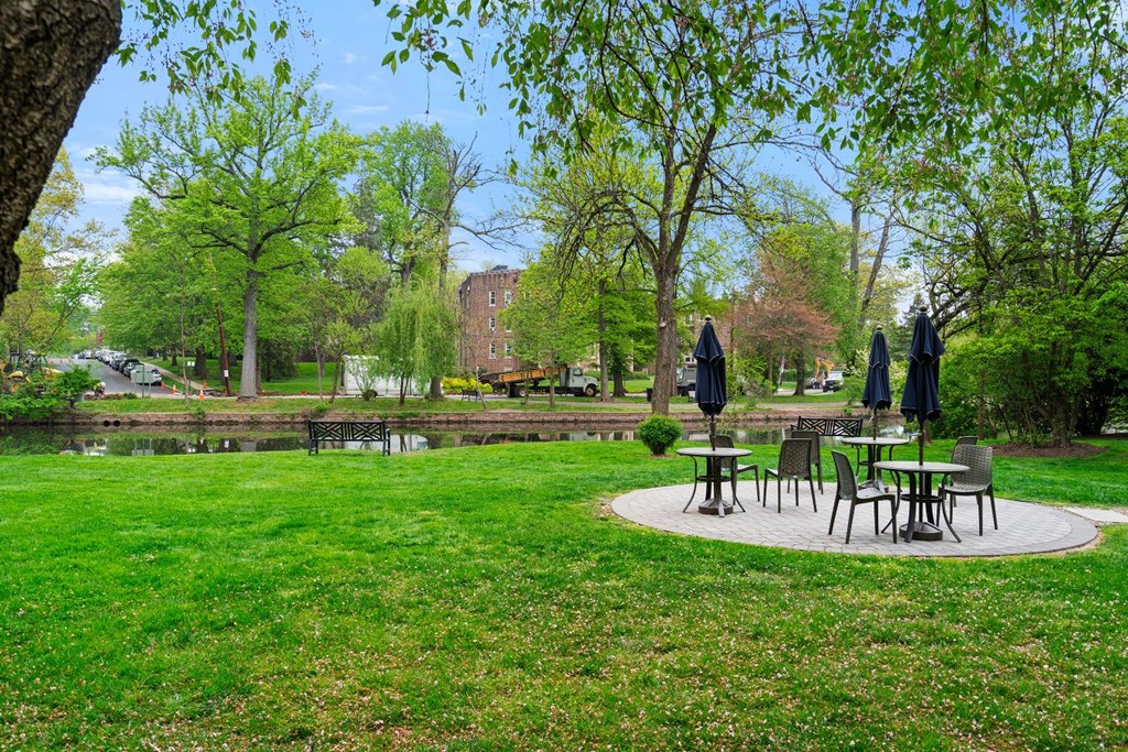 a park with tables and umbrellas next to a pond