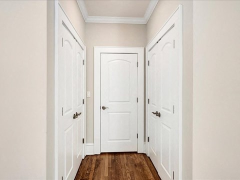 A hallway with three doors and wooden floors.