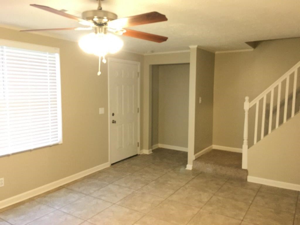 an empty living room with a ceiling fan and a staircase