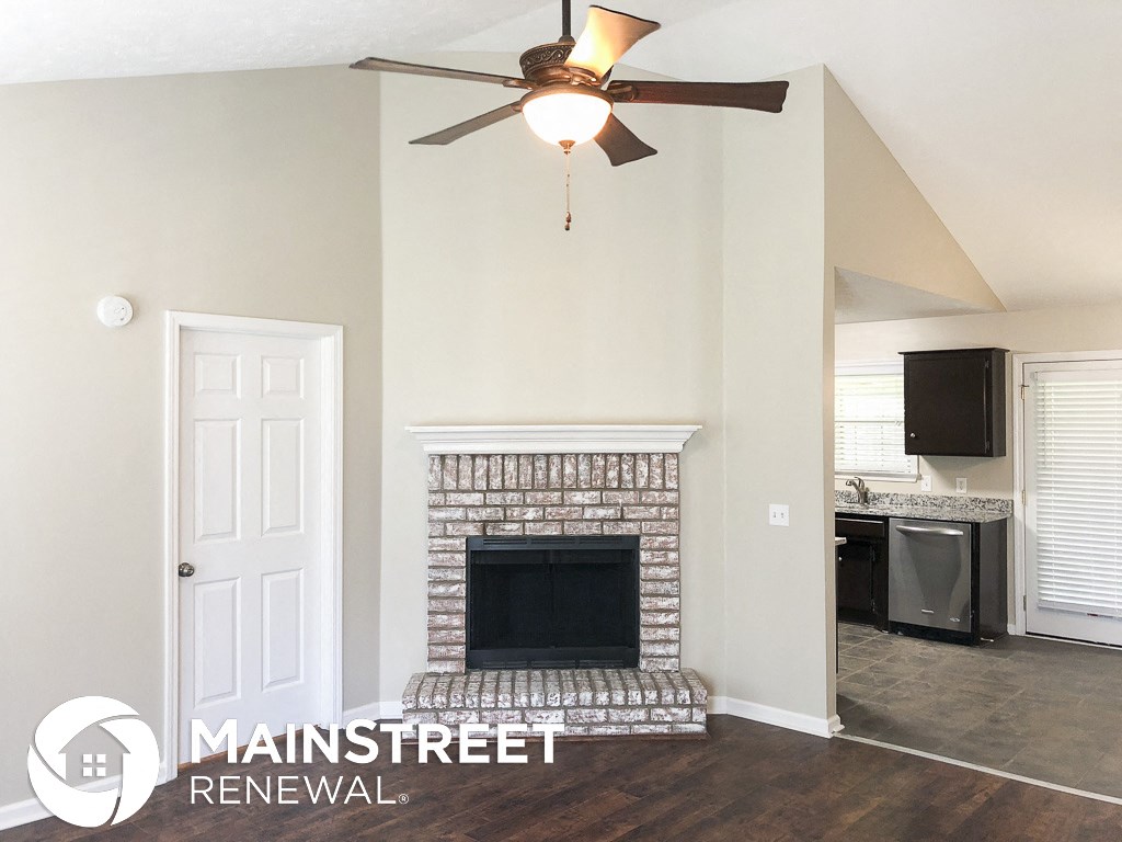 a renovated living room with a brick fireplace and a ceiling fan