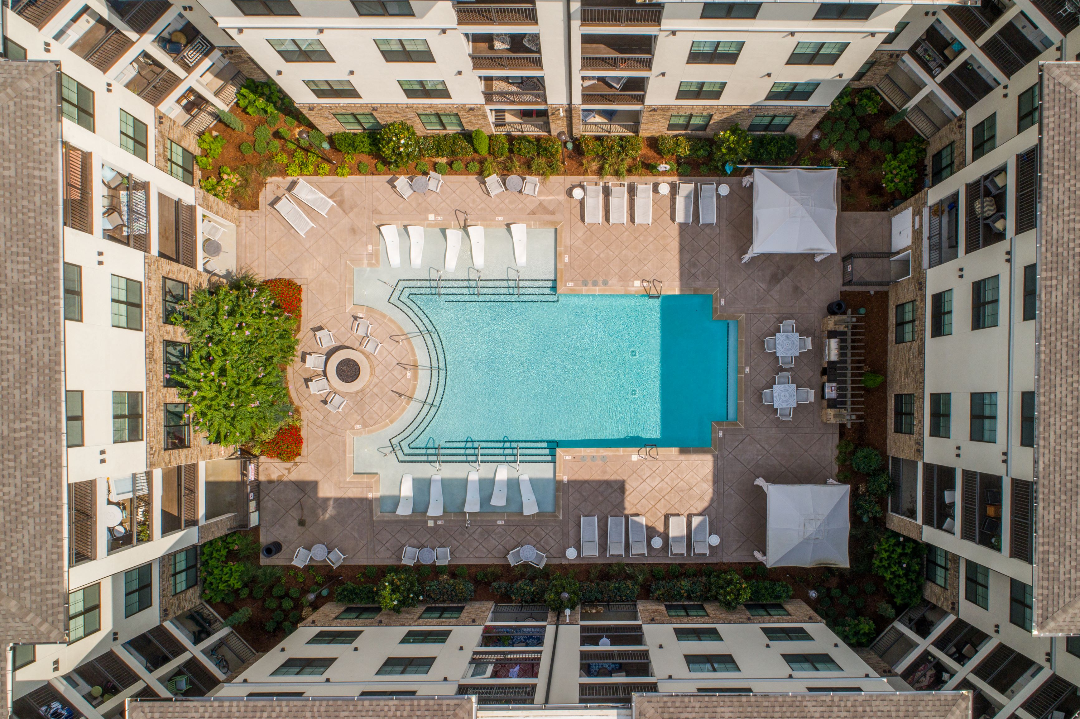 A swimming pool surrounded by lounge chairs and trees in a courtyard.