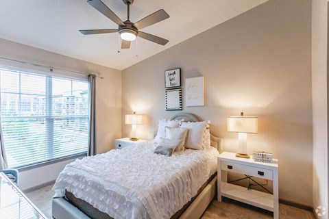 A bedroom with a large bed, a ceiling fan, and two lamps.
