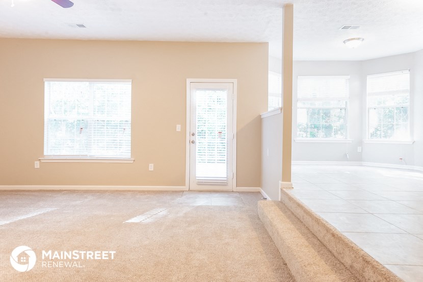 an empty living room with a staircase and a door to the dining room