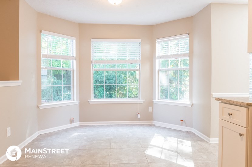 an empty dining room with three windows and a tile floor