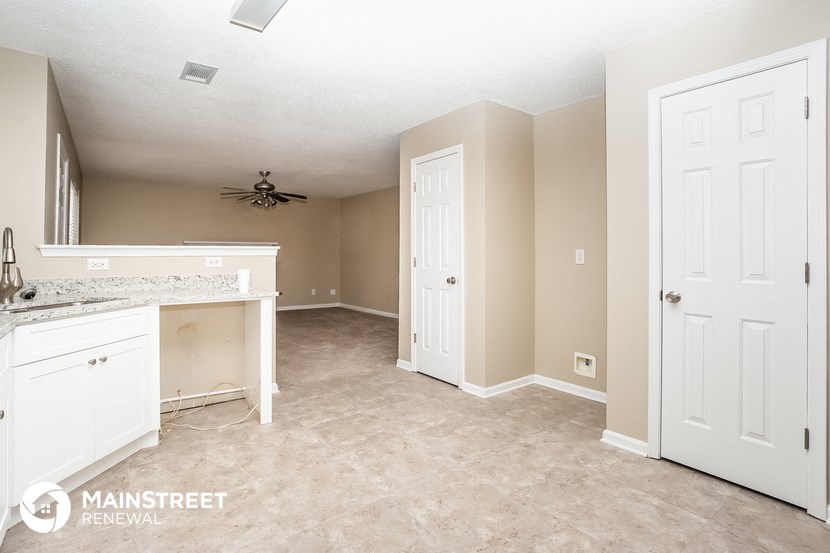 the kitchen and living room of a home with white cabinets and beige walls