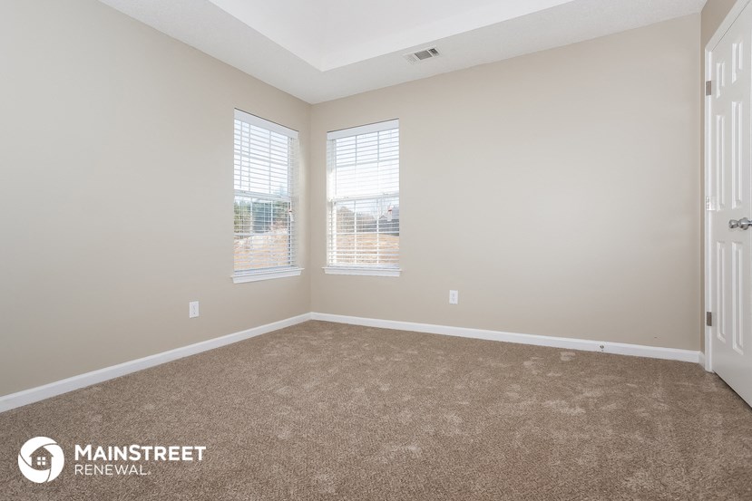 the spacious living room with two windows and carpeting